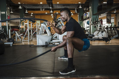 Muscular sportsman exercising with rope during sports training in gym