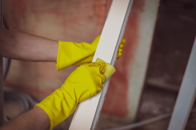 Hands of a young caucasian man in yellow rubber gloves washes window frames with a sponge and soap