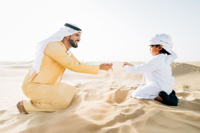 Father and son enjoying while kneeling in desert