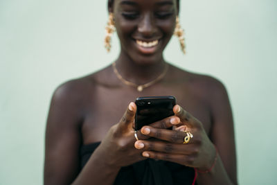 Young woman using mobile phone while standing against green wall