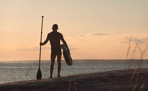 Silhouette man standing by sea against sky during sunset