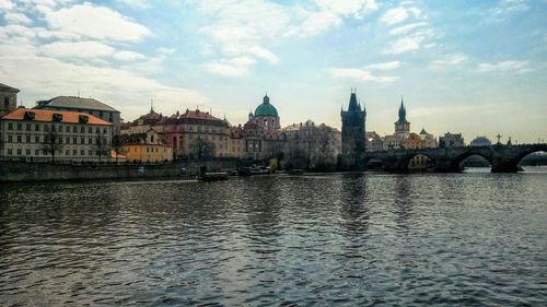 View of buildings by river against cloudy sky