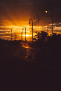 Silhouette trees by road against orange sky