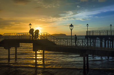 Silhouette people on pier by sea against sky during sunset