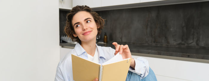 Portrait of smiling young woman standing against wall