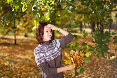Happy caucasian young woman in a sweater holds bright autumn colors in her hand