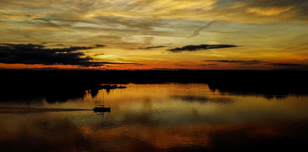 Scenic view of lake against dramatic sky during sunset
