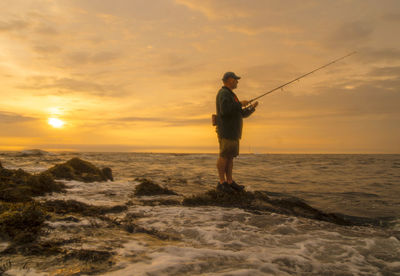 Maine coastal fisherman waits for a striped bass to bite as sun rises.