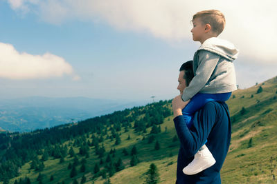 Father and son on mountain against sky