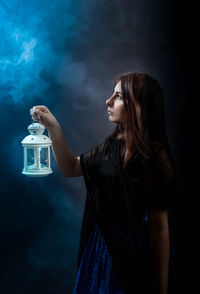 Woman holding lit lantern while standing by wall