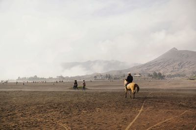 People riding horses on landscape against sky