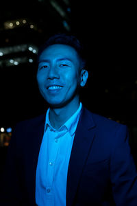 Positive asian male in formal wear looking at camera on street in night time with blue neon light