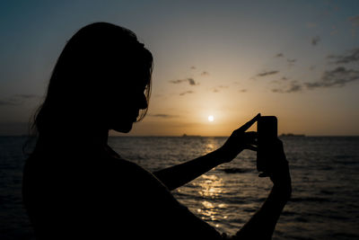 Silhouette woman sitting on beach against sky during sunset