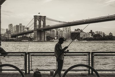 Man standing on bridge over river in city against sky