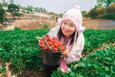 Portrait of smiling young woman holding strawberries in bucket