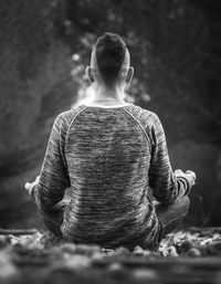 Rear view of man sitting in lotus position on field