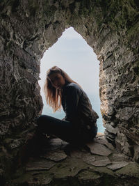 Portrait of woman sitting in old rocky window by sea