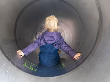 Blond girl with arms outstretched playing in tube slide at playground