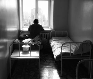 Rear view of man on bed looking through window in hospital