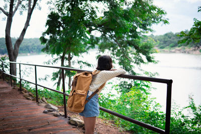Rear view of woman walking by railing against trees