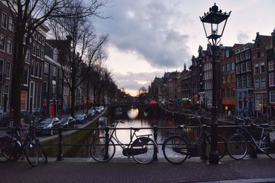 Bicycles on street by canal against sky in city