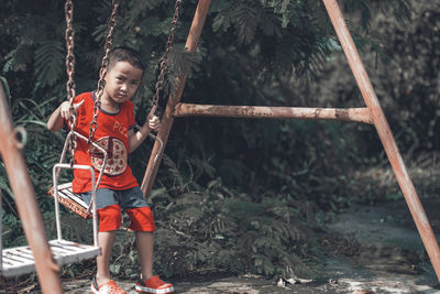 Portrait of smiling boy on swing against trees