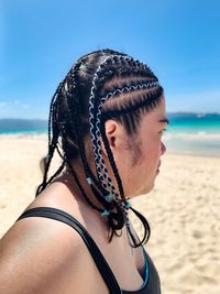 Side view of woman with braided hair standing at beach against clear sky