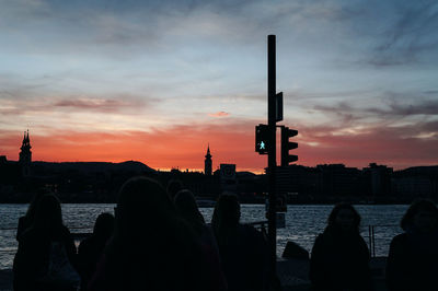 Silhouette people on building against cloudy sky during sunset