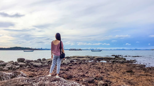 Rear view of woman standing on beach against sky