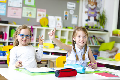 Girls with hands raised at table in classroom