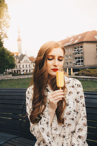 Portrait of young woman holding sunglasses against built structure