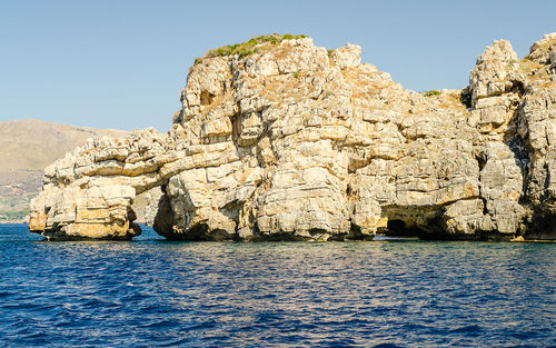 Rocks by sea against clear blue sky