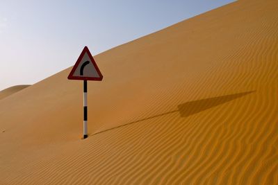 Road sign in desert against clear sky