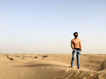 Full length of shirtless man standing in desert against clear sky