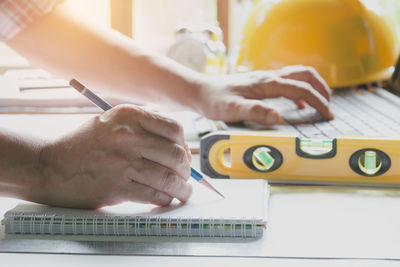 Cropped hands of engineer writing in book at office