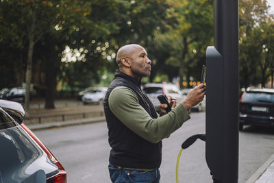 Side view of man scanning and paying through smart phone while standing at charging station