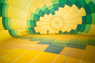 Unrecognizable man checking condition of large green and yellow air balloon while standing inside and conducting maintenance