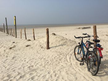 Bicycles parked on sand at beach against sky