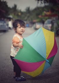 Portrait of cute baby girl holding colorful umbrella while standing on road