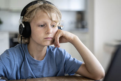 Boy with wired headphones leaning on elbow at table