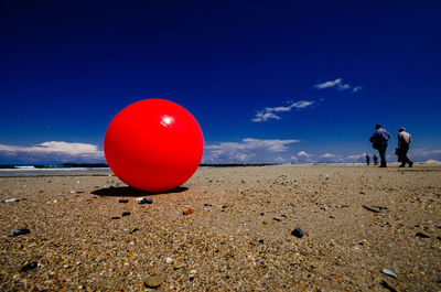 Red ball at beach against blue sky