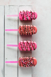 A row of decorated cakesicles for valentine's day, on a white wooden board.