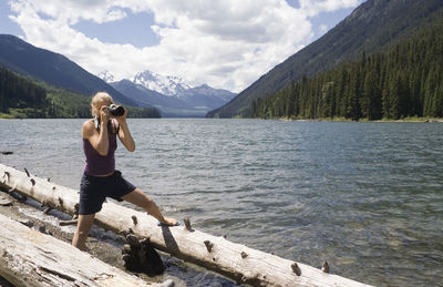 Full length of woman photographing through digital camera at lakeshore