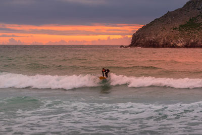 Man surfing in sea against sky during sunset