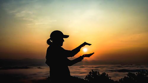 Silhouette man with arms outstretched against sunset sky