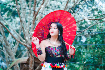 Young woman looking away while standing against trees