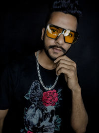 Portrait of young man wearing sunglasses against black background