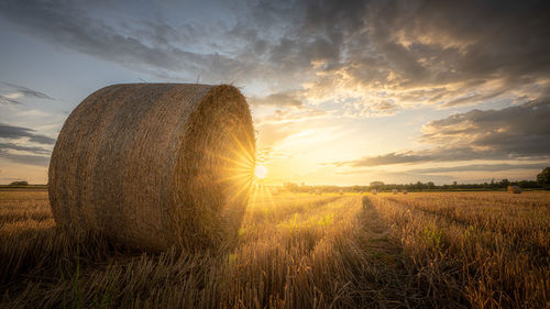 Hay bales on field against sky during sunset