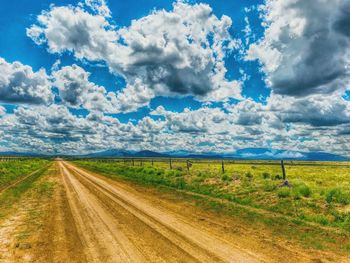 Dirt road amidst field against sky