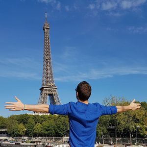 Rear view of man standing in front of eiffel tower against blue sky